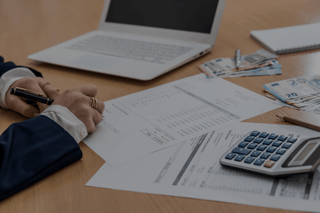 Persona trabajando con facturas, calculadora, euros y portátil sobre una mesa, en un contexto de asesoramiento contable.