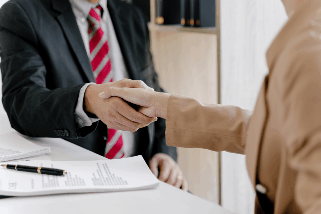 Dos personas estrechando la mano en una oficina de asesoría integral tras firmar documentos, representando un acuerdo de asesoría de empresas y autónomos.