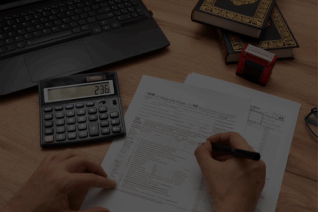 Persona rellenando formularios con calculadora y ordenador portátil durante la declaración de la renta.